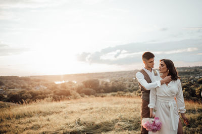 Young couple standing against sky during sunset