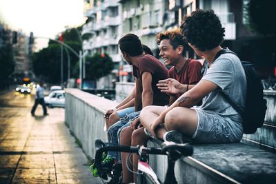 Friends sitting by street on retaining wall in city