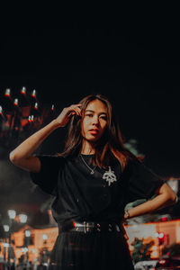 Portrait of young woman standing against black background