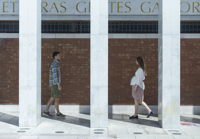 Side view of two people walking against building