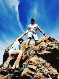 Low angle view of people on rock against sky