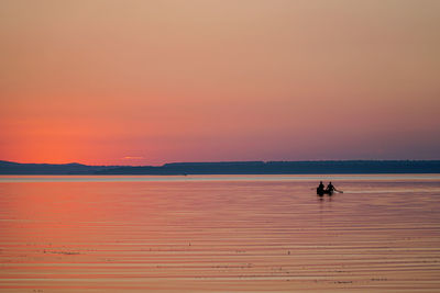 Silhouette people on boat in sea against orange sky