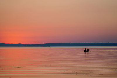 Silhouette people on boat in sea against orange sky