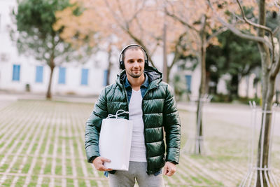 Mid adult man holding bag looking away while standing outdoors