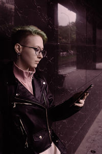 Portrait of a teenager girl using the mobile phone against black ceramic tile walls