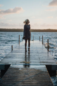 Woman walking on pier over lake against sky