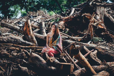 Portrait of young woman sitting on logs in forest