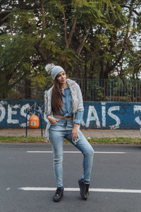 Full length portrait of young woman standing on road