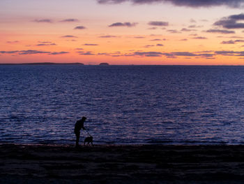 Silhouette people on beach against sky during sunset