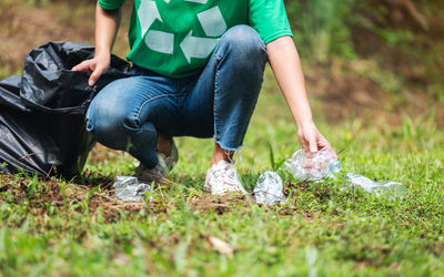 A female activist picking up garbage plastic bottles into a plastic bag in the park 