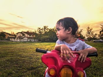 Boy sitting on field against sky during sunset