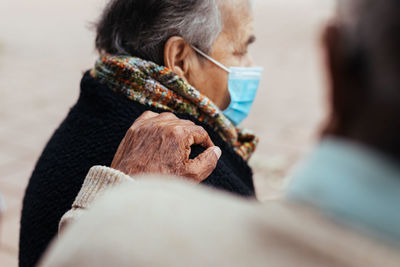 Side view of elderly couple sitting on a park bench while the husband puts his hand on his wife's shoulder in a gesture of love