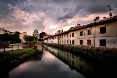 River amidst houses and buildings against sky at sunset