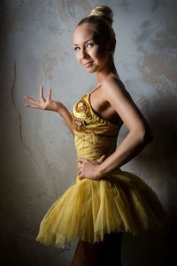 Portrait of beautiful ballerina standing while gesturing against wall in dark