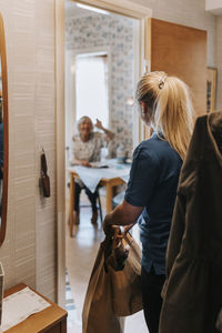 Female caregiver with bags looking at senior woman sitting at home