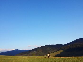 Woman walking on grassy field by mountains against sky
