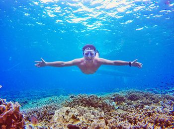 Happy shirtless man swimming undersea