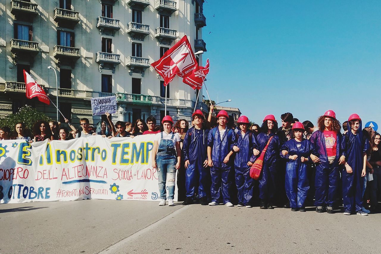 large group of people, patriotism, real people, flag, men, pride, text, women, day, outdoors, protestor, togetherness, clear sky, architecture, building exterior, crowd, city, adult, people