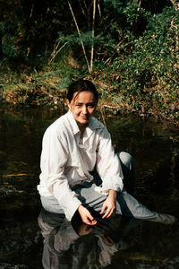 Portrait of smiling young woman sitting in lake at forest 