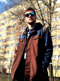 Young man wearing sunglasses standing against building in city