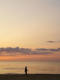 Woman walking at beach against sky during sunset