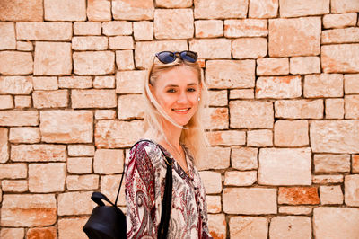 Portrait of smiling woman standing against stone wall