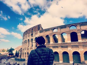 Rear view of man standing by coliseum against sky