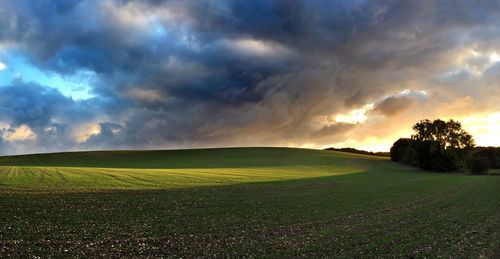 Scenic view of field against dramatic sky at sunset