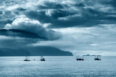 Silhouette boats reefnet fishing amidst sea against cloudy sky