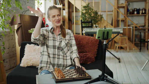 Smiling woman gesturing while sitting by chess board