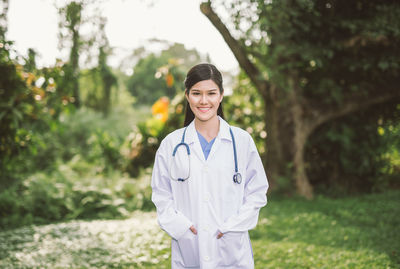 Portrait of female doctor wearing lab coat while standing at park