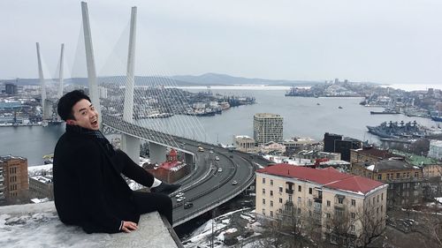 Young woman sitting on buildings against sky in city