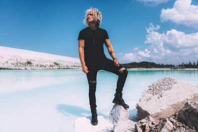 Full length of man standing on rock by lake against sky