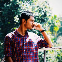 Young man drinking glass while standing by tree