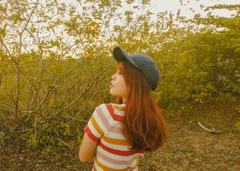 Rear view of woman wearing cap while standing against plants