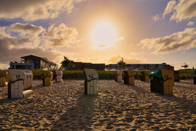 Hooded beach chairs on sand against sky during sunset