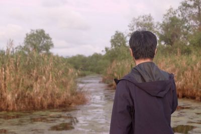 Rear view of man standing by river against sky