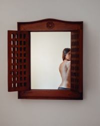 Rear view of shirtless woman standing against wall at home