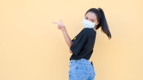 Portrait of young woman standing against yellow background