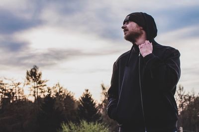 Man looking away while standing against sky during sunset