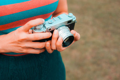 Midsection of woman holding camera while standing outdoors