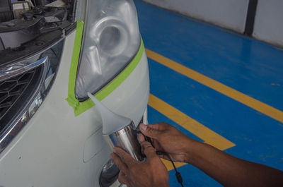 Cropped hand of mechanic spraying water on headlight