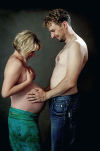 Side view of shirtless man standing against black background