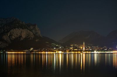 Illuminated lake by mountains against clear sky at night