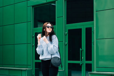 Young woman using mobile phone while standing against building