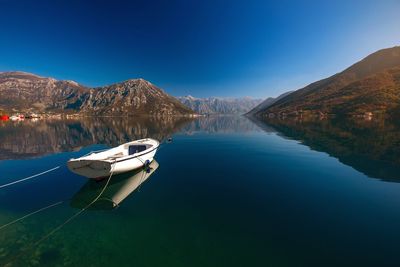 Boats moored on lake against clear blue sky