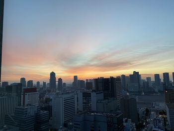 Modern buildings in city against sky during sunset