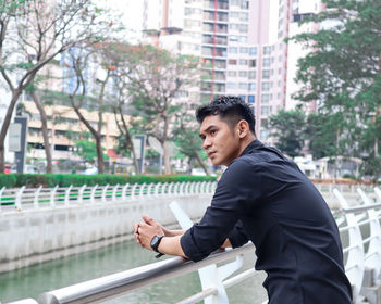 Thoughtful young man standing against canal in city