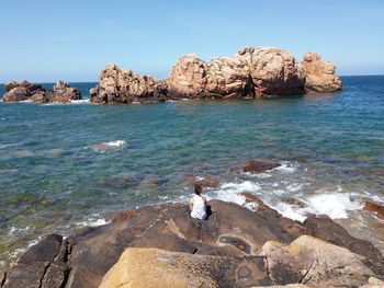 Man on rock by sea against sky