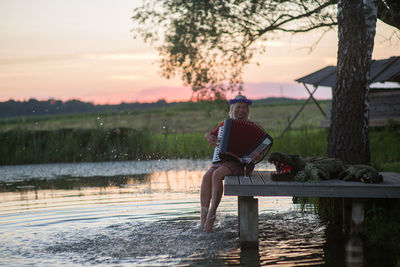 Woman playing accordion on pier during sunset